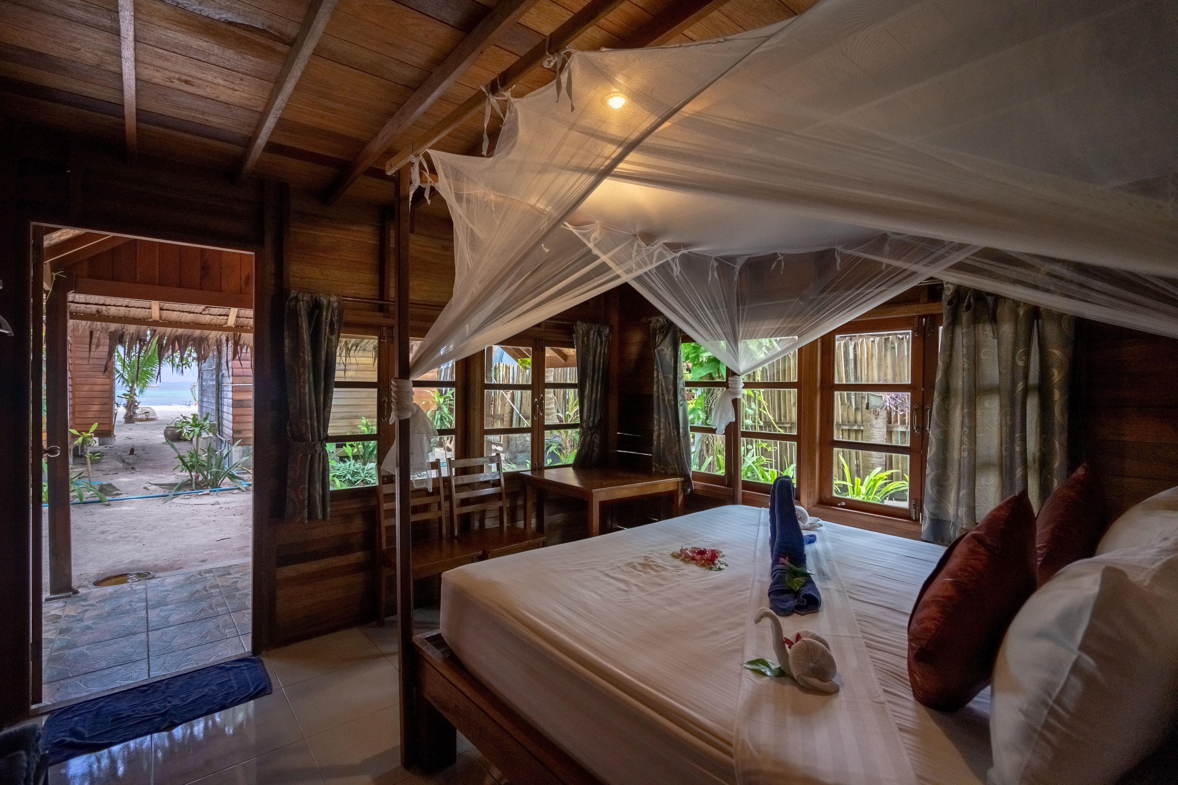 A wooden room with a bed, a desk, and a window overlooking a garden.
