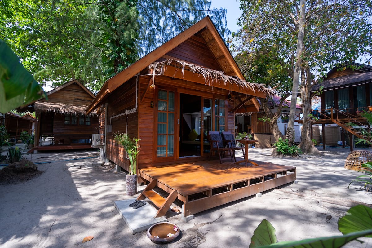 Uma cabana de madeira com telhado de palha, um deck de madeira e chão arenoso.