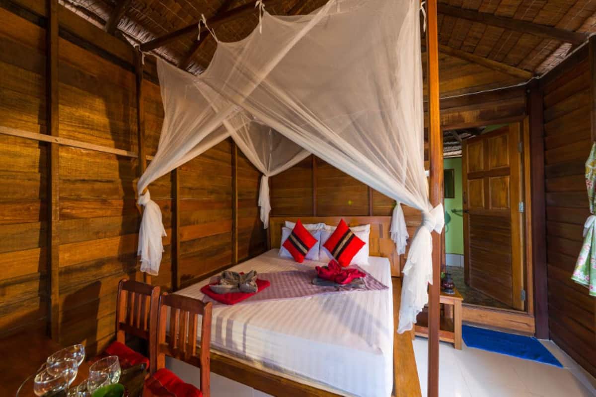 Um quarto de madeira com uma cama, uma mesa com copos e um banco.