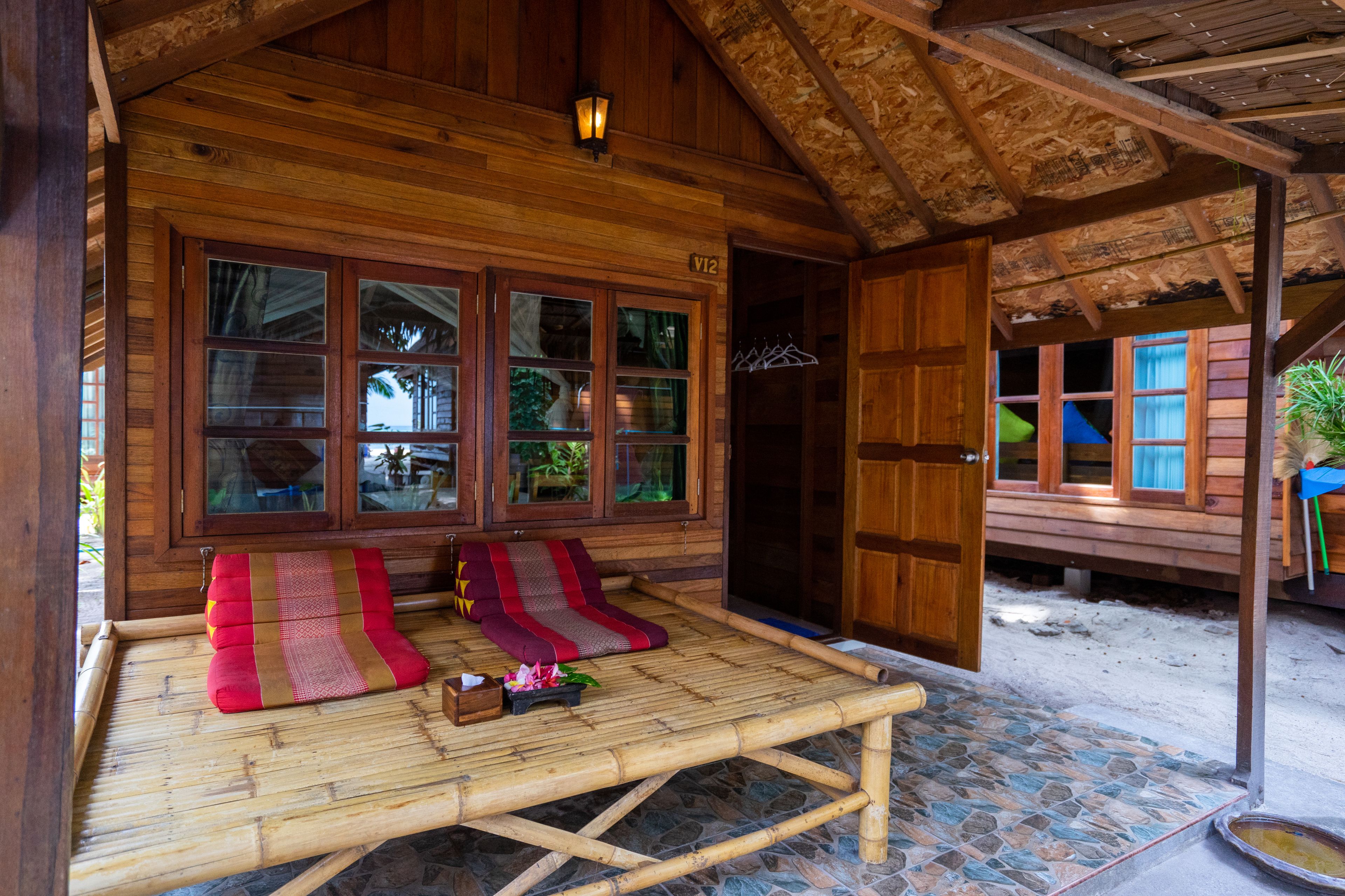 A wooden cabin with a large window, a bamboo mat, and a small table with a plant.