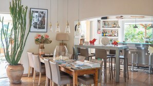Un coin repas avec une table en bois, des chaises et un cactus. Il y a également un bar avec des tabourets et une étagère remplie de bouteilles.