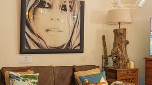 Un salon avec un canapé en cuir marron, une œuvre d’art encadrée, une lampe en bois et une table basse sur laquelle se trouvent un bol et des télécommandes.