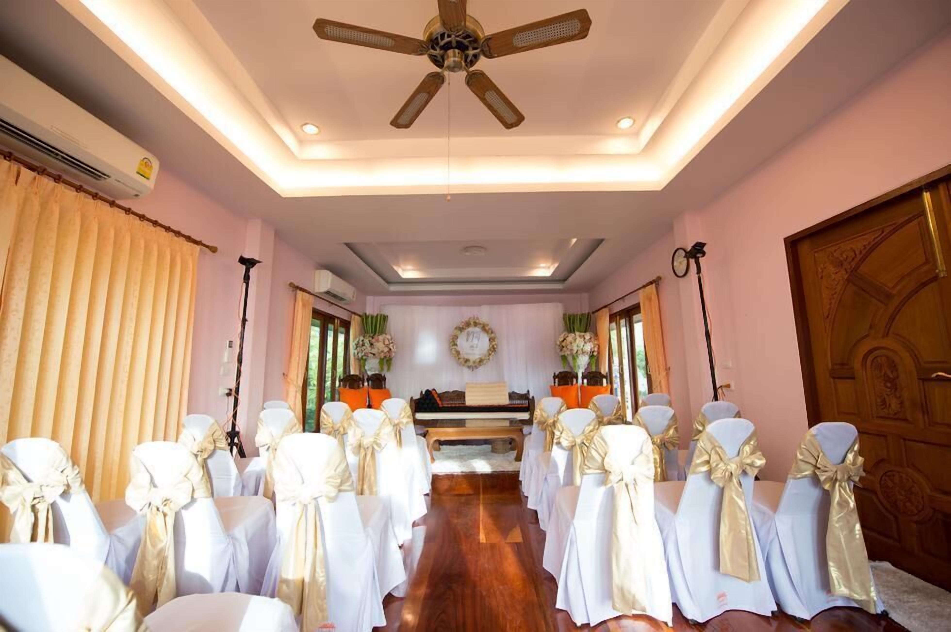 A wedding ceremony area with rows of white chairs with gold sashes, a wooden piano, and a ceiling fan.