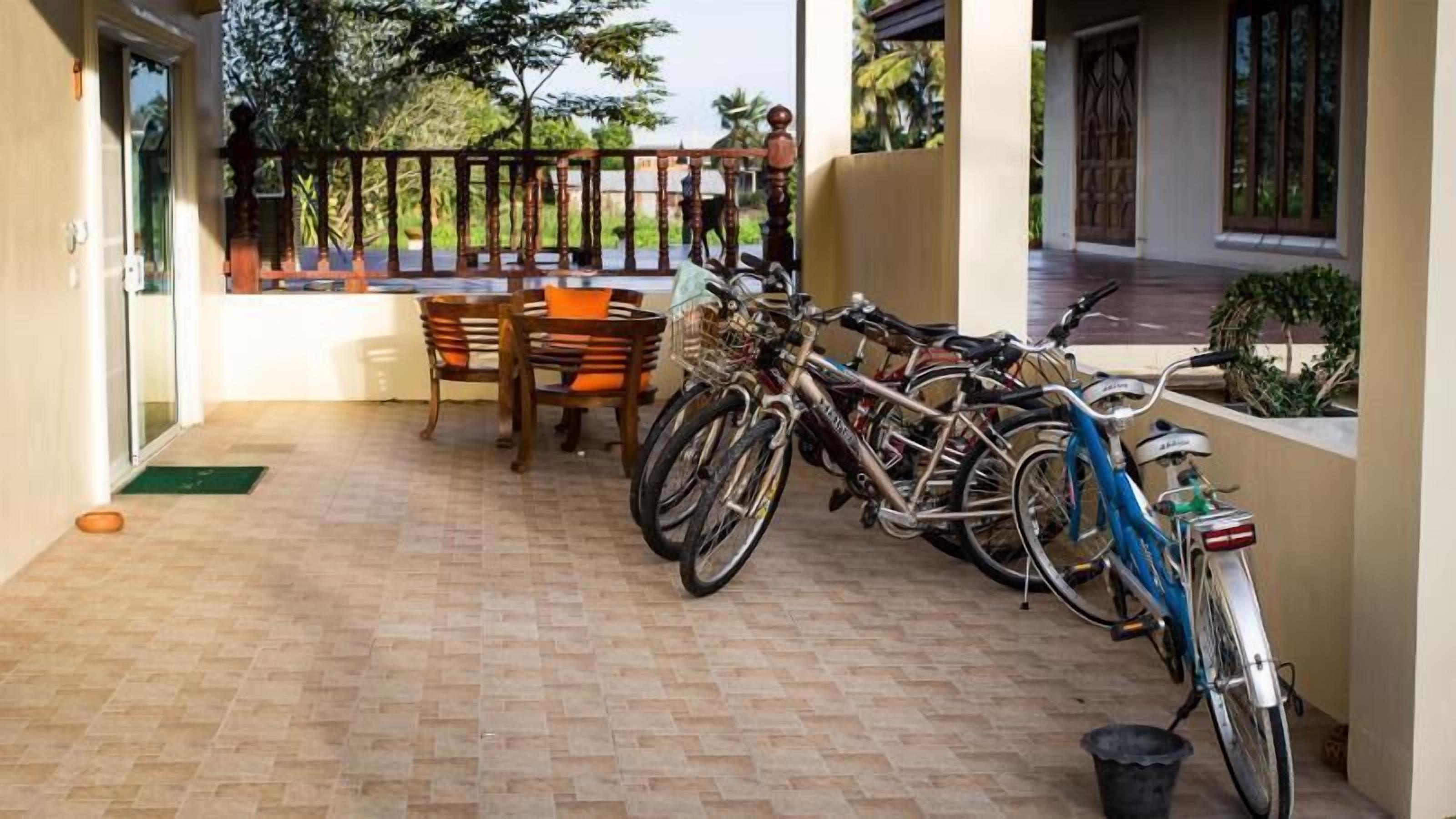 Un balcón con suelo de baldosas, sillas de madera, una mesa y un aparcamiento para bicicletas con varias bicicletas.