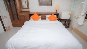 A hotel room with a large bed, two orange pillows, a nightstand with a lamp, a wooden wardrobe, and a painting on the wall.