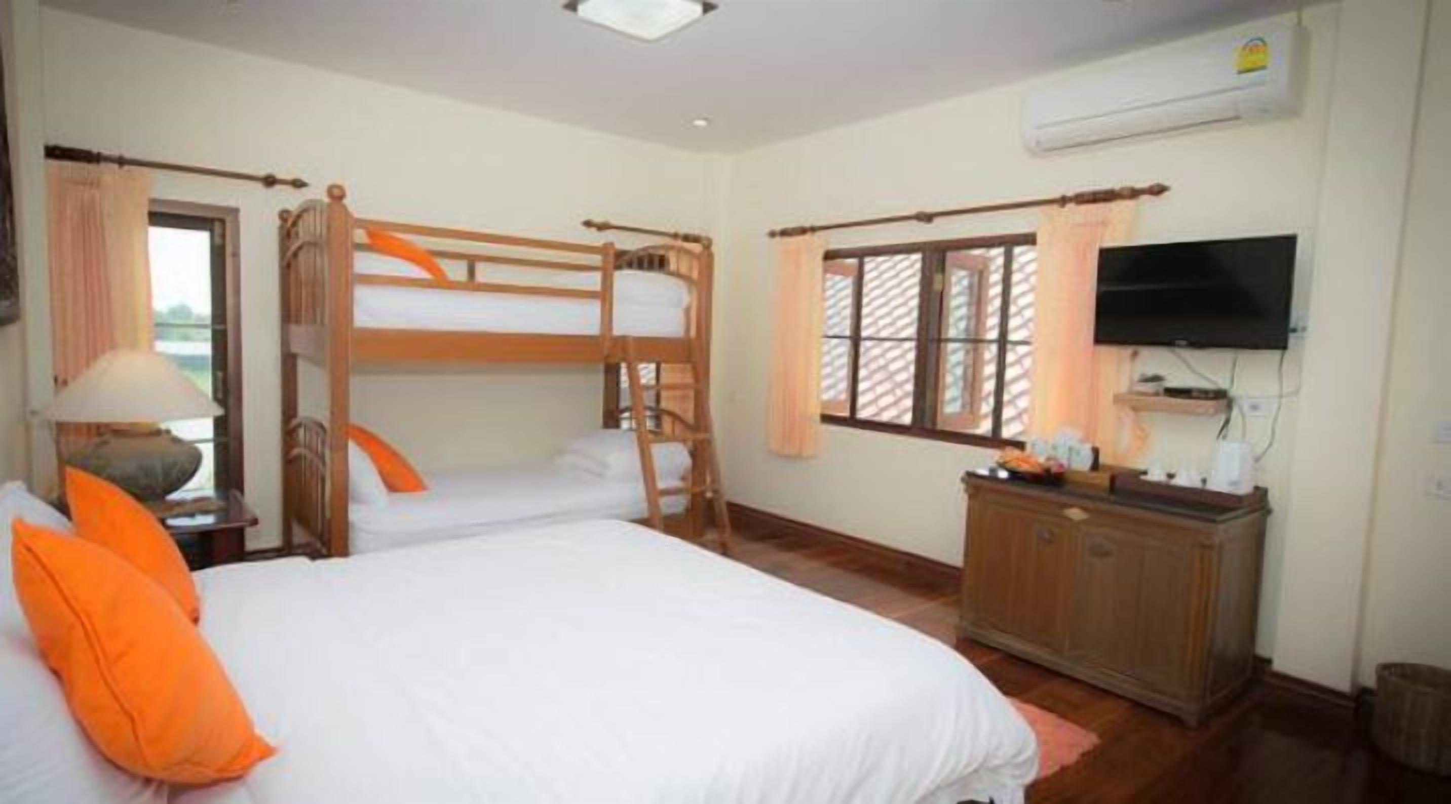 Une chambre avec un lit superposé, un bureau avec une chaise, un téléviseur fixé au mur et une fenêtre avec des rideaux.
