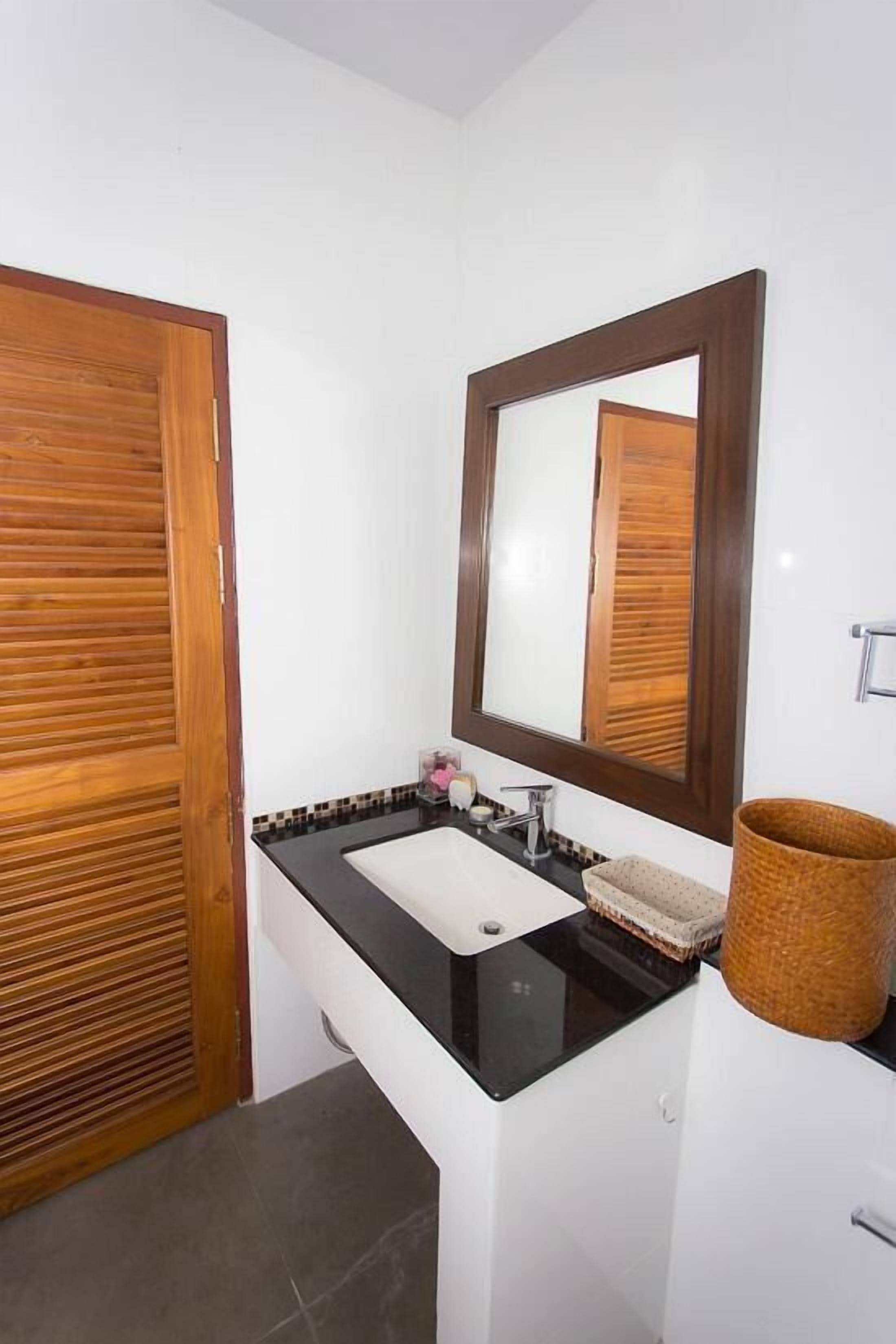 A bathroom with a wooden door, a black sink, a mirror, and a woven basket.