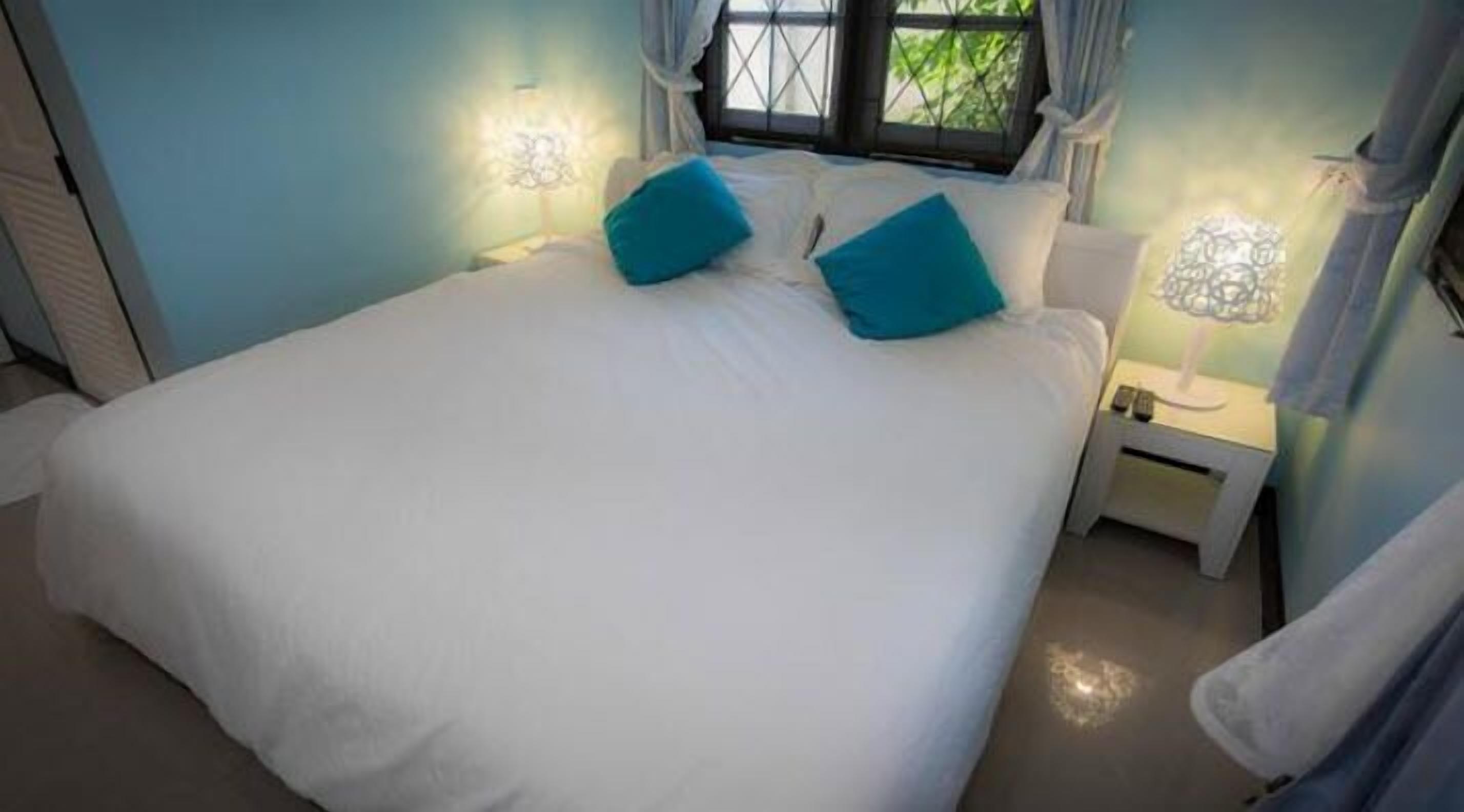 A bedroom with a large bed, two pillows, a nightstand with a lamp, and a window with curtains.