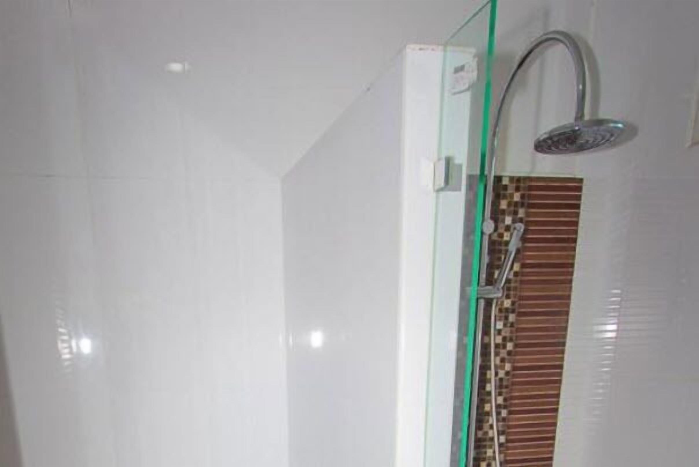 Une salle de bain moderne avec une douche à paroi de verre, un mur recouvert de carreaux blancs et un pare-chocs en carreaux décoratifs.