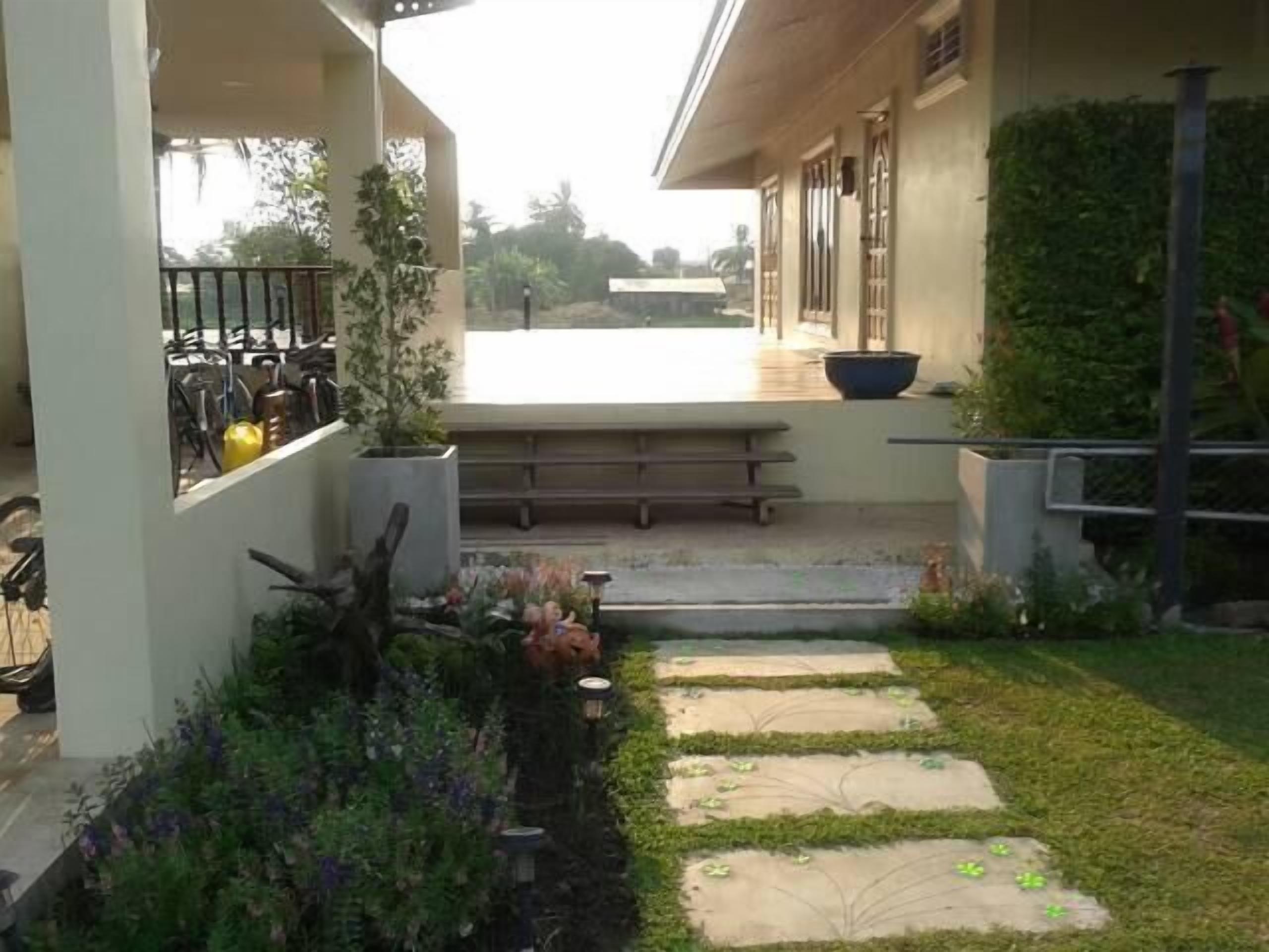 A covered outdoor area with a bench, potted plants, and a pathway leading to a building.