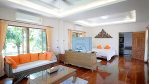 A spacious living area with a sofa, a coffee table, a TV, and a bed with orange pillows.