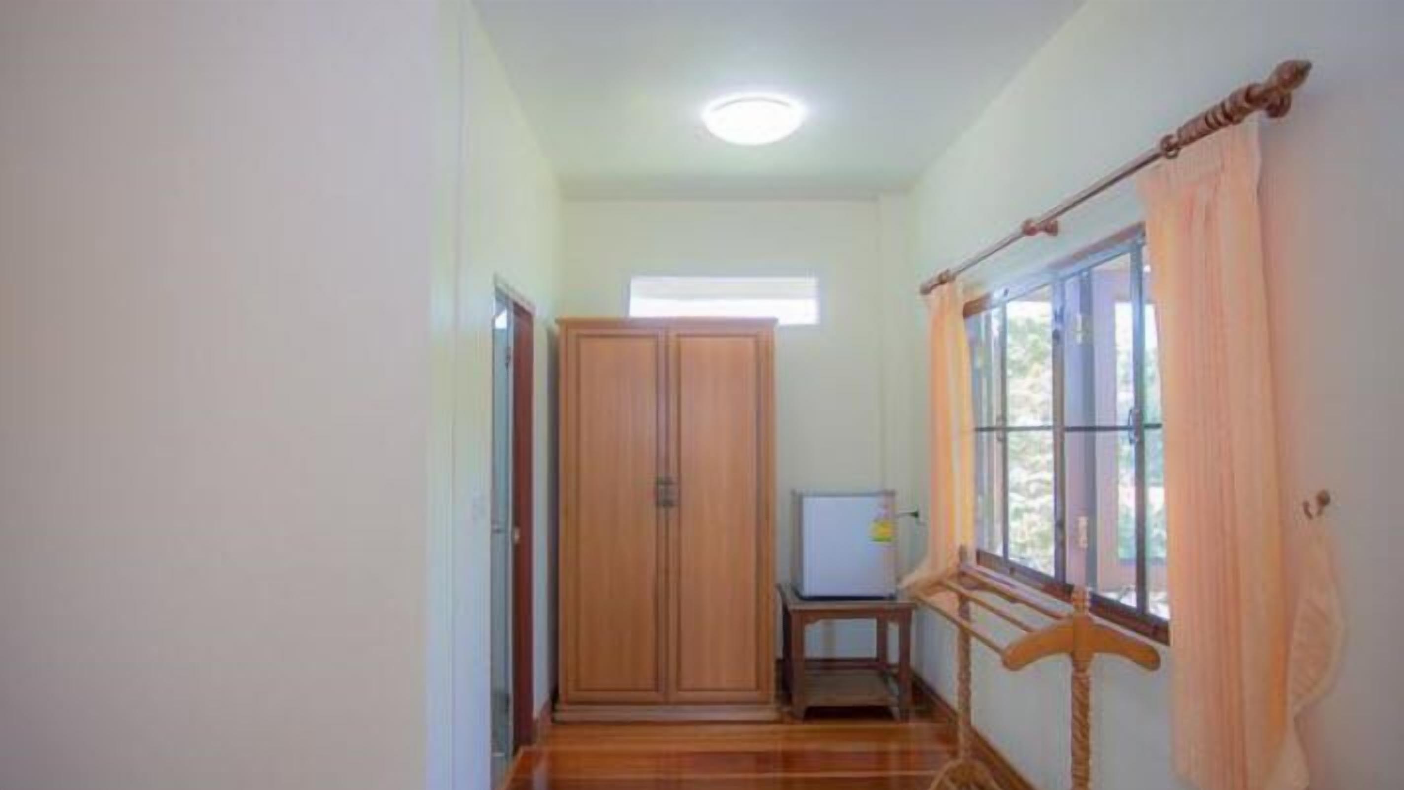 A room with a wooden wardrobe, a small table, and a window with curtains.