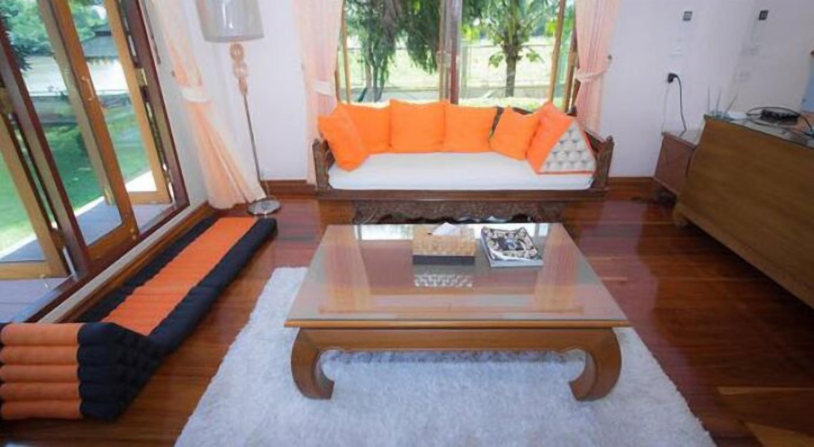 A room with a sofa, a glass coffee table, and a view of greenery outside.