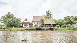 A two-story house with a tiled roof, surrounded by water and greenery.