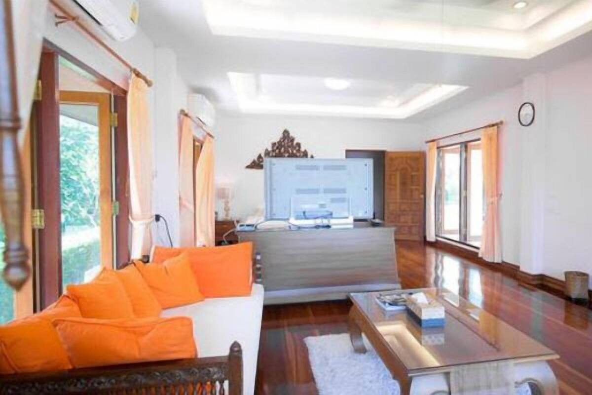 Ein geräumiges Zimmer mit einem großen Bett, einem Sofa mit orangefarbenen Kissen, einem Holztisch und einem großen Fenster.