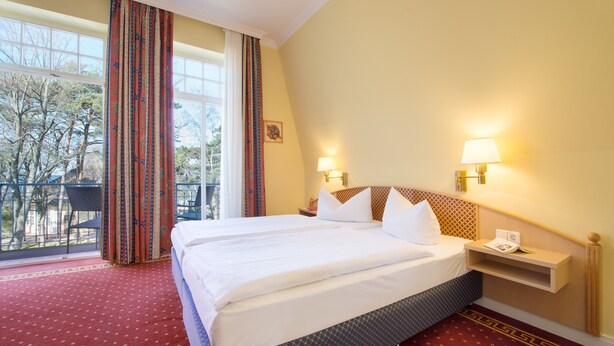 Hotelkamer met een groot bed, twee bedlampjes, een klein nachtkastje en uitzicht op bomen door het raam.