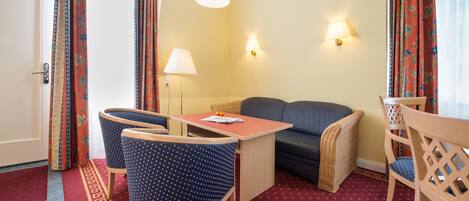Habitación de hotel con sofá, dos sillones, una mesa y dos lámparas de pared.