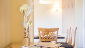 Een tafel met een bloevas, een stapel tijdschriften en een houten stoel in een kamer met een lamp en een raam.