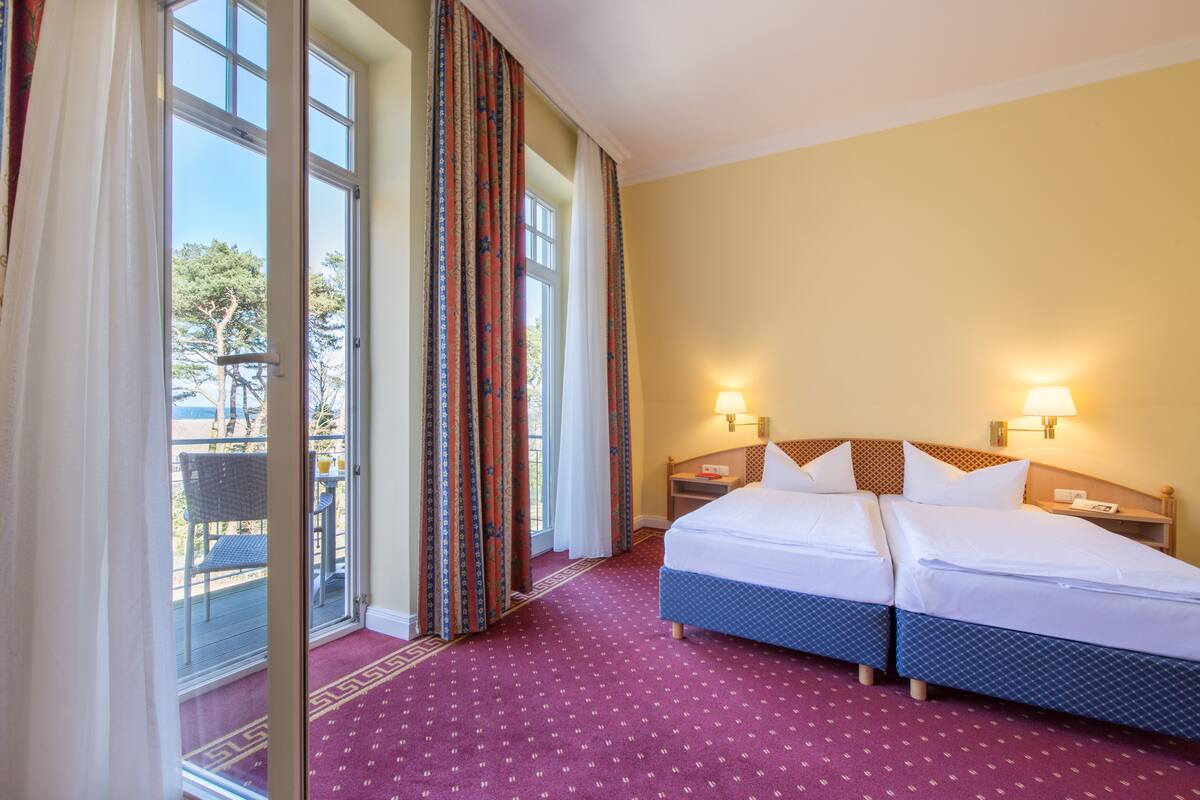 Ein Hotelzimmer mit zwei Betten, einem Balkon und großen Fenstern.