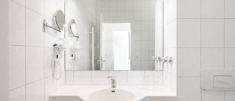 A modern bathroom with a white sink, two mirrors, a towel rack, and a toilet.