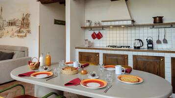 A dining area with a table set for two, a kitchen with white tiles and wooden cabinets, and a mural on the wall.