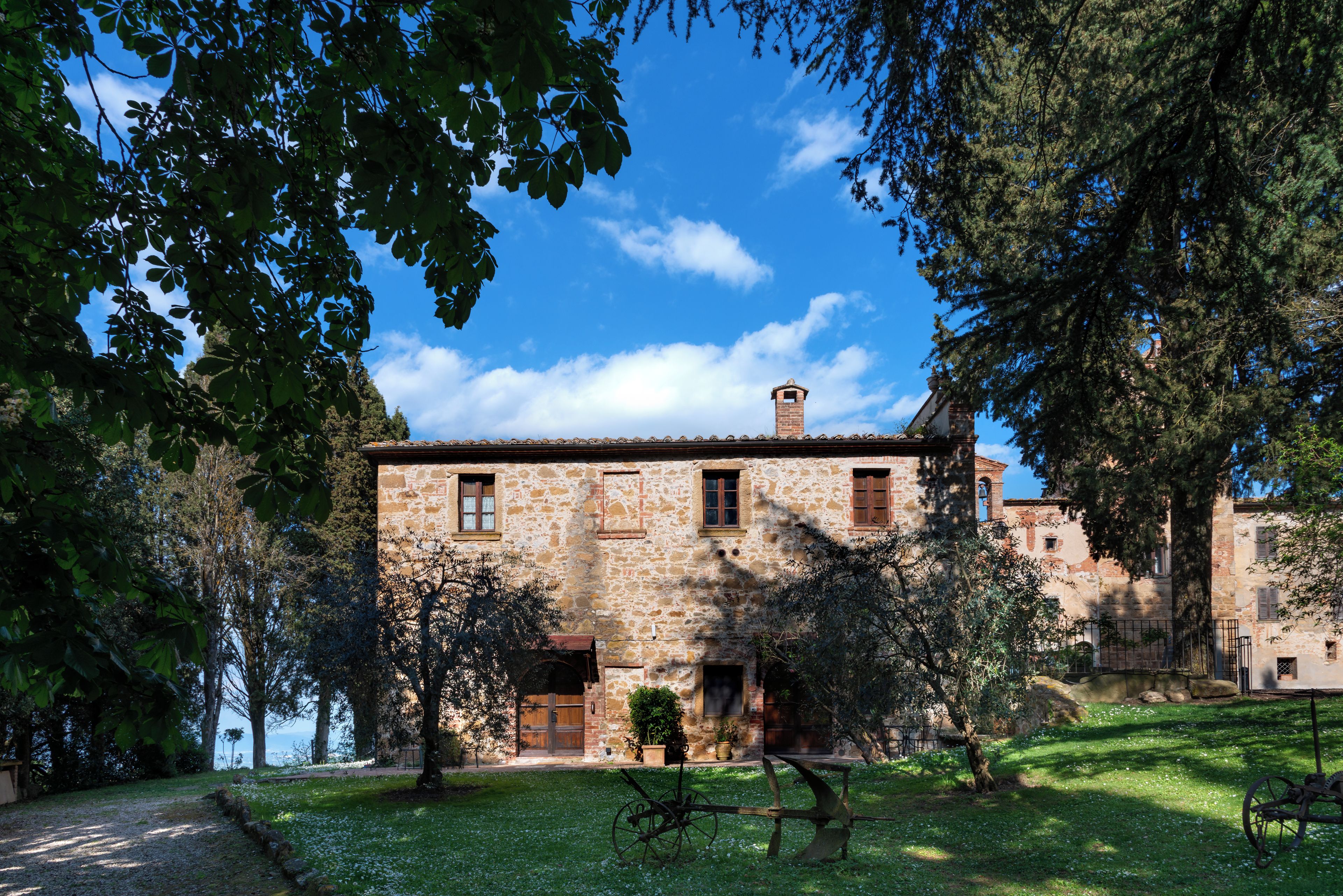 A stone building with a traditional design, featuring a wooden door and windows, surrounded by lush greenery and a clear blue sky.