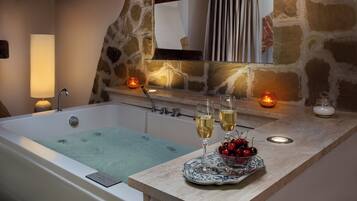 A bathroom with a bathtub, a mirror, and a countertop with two glasses of white wine and a bowl of cherries.