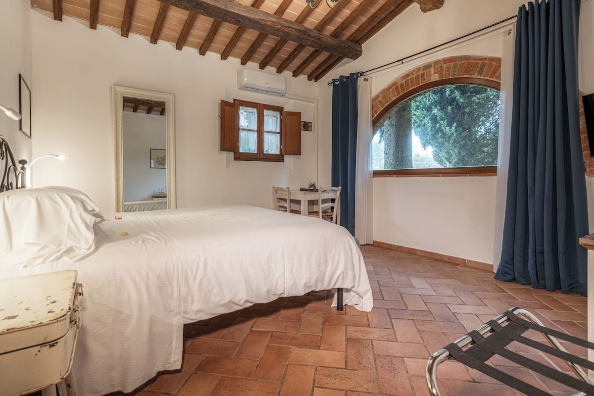 A bedroom with a bed, a desk, a chair, a mirror, and a window with curtains.