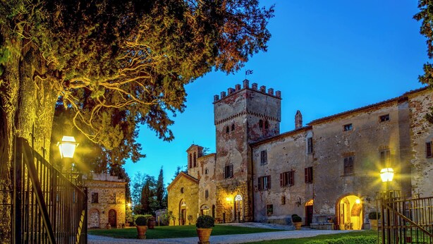 A historic building with a tower, a courtyard, and a well-lit entrance. - Abbadia Sicille Relais (Trequanda)