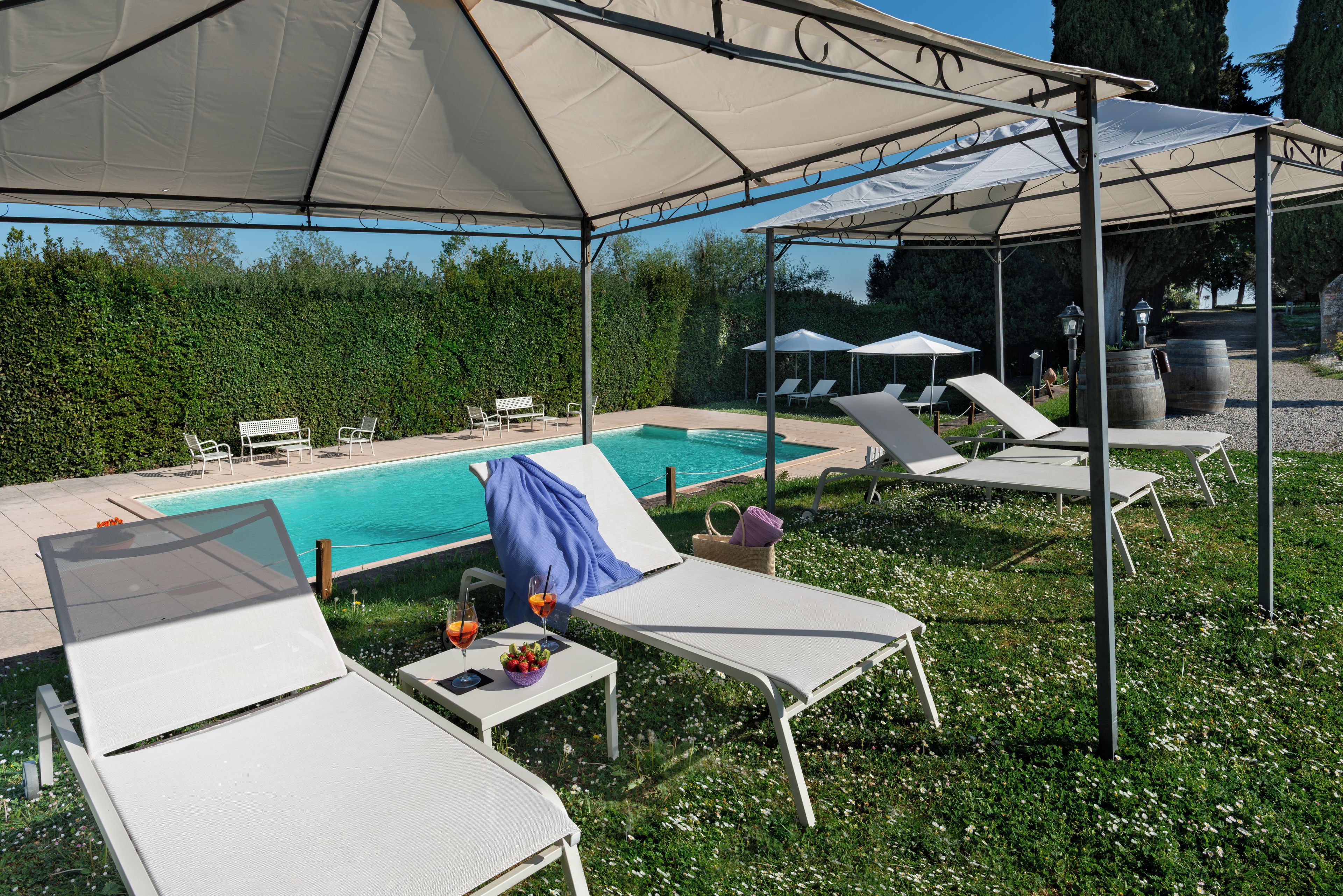 A poolside area with lounge chairs, a table with drinks, and umbrellas providing shade.