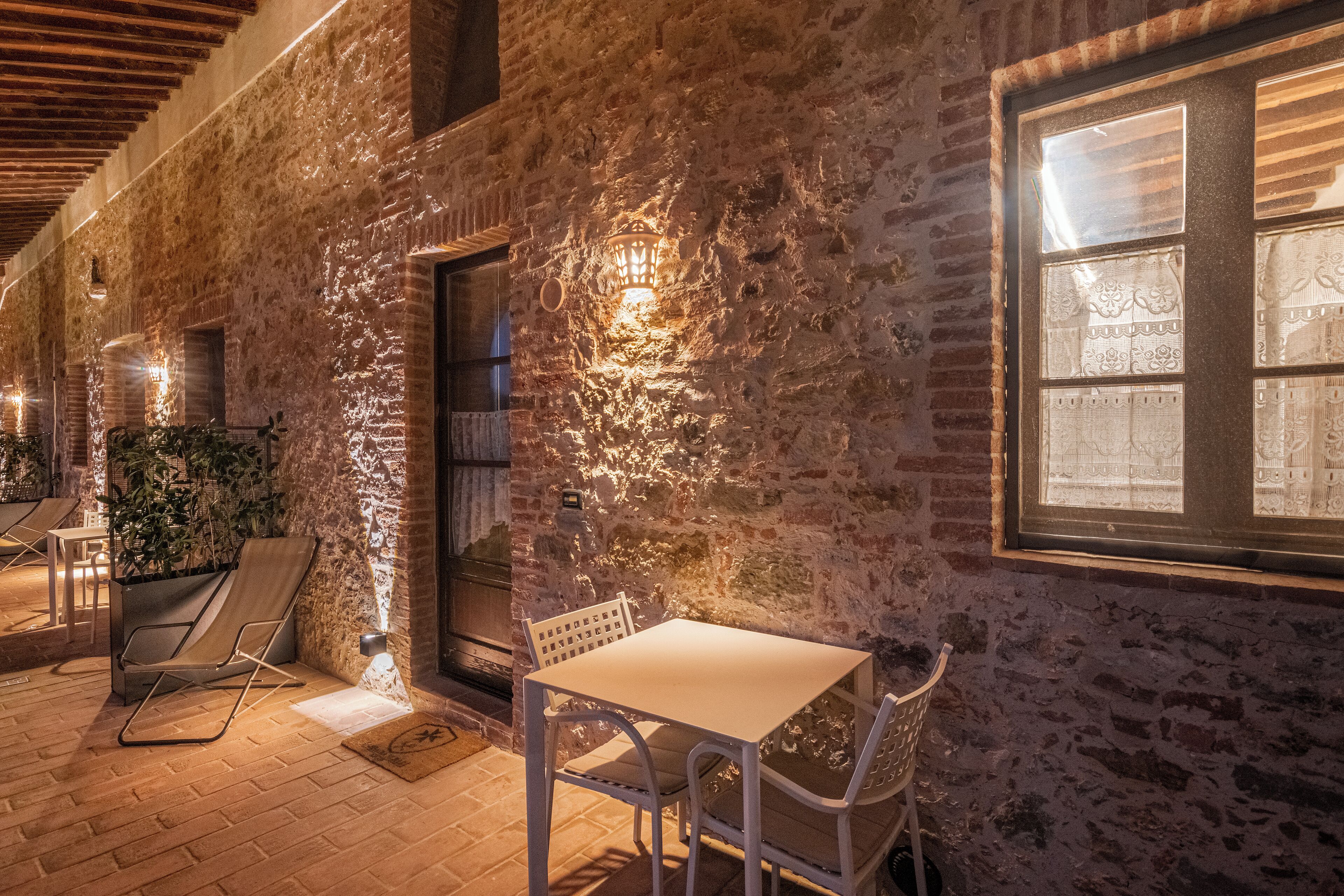 An outdoor patio with a brick wall, a table, chairs, and a potted plant.
