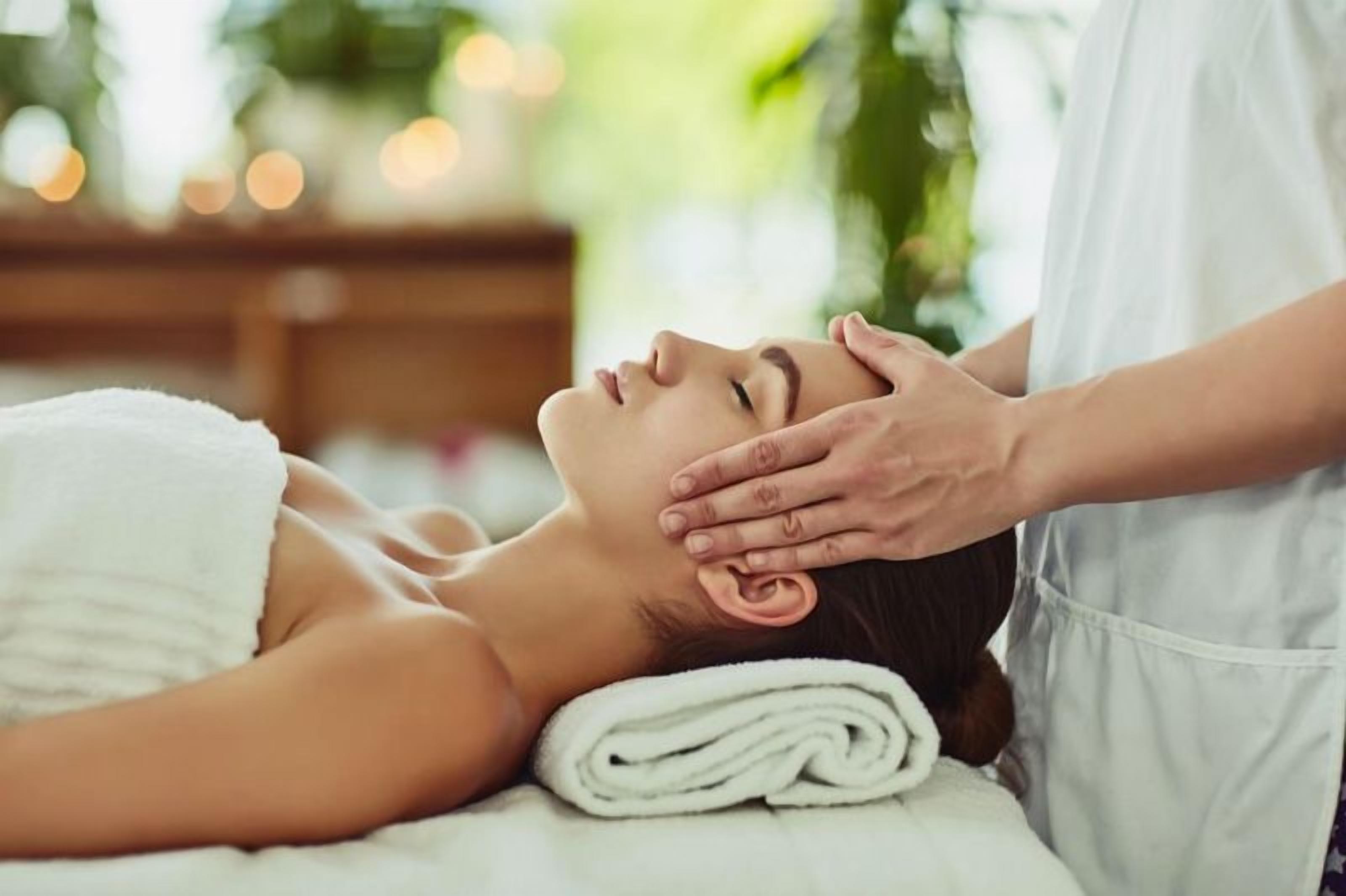 A person receiving a massage in a room with a wooden floor and a plant in the background.