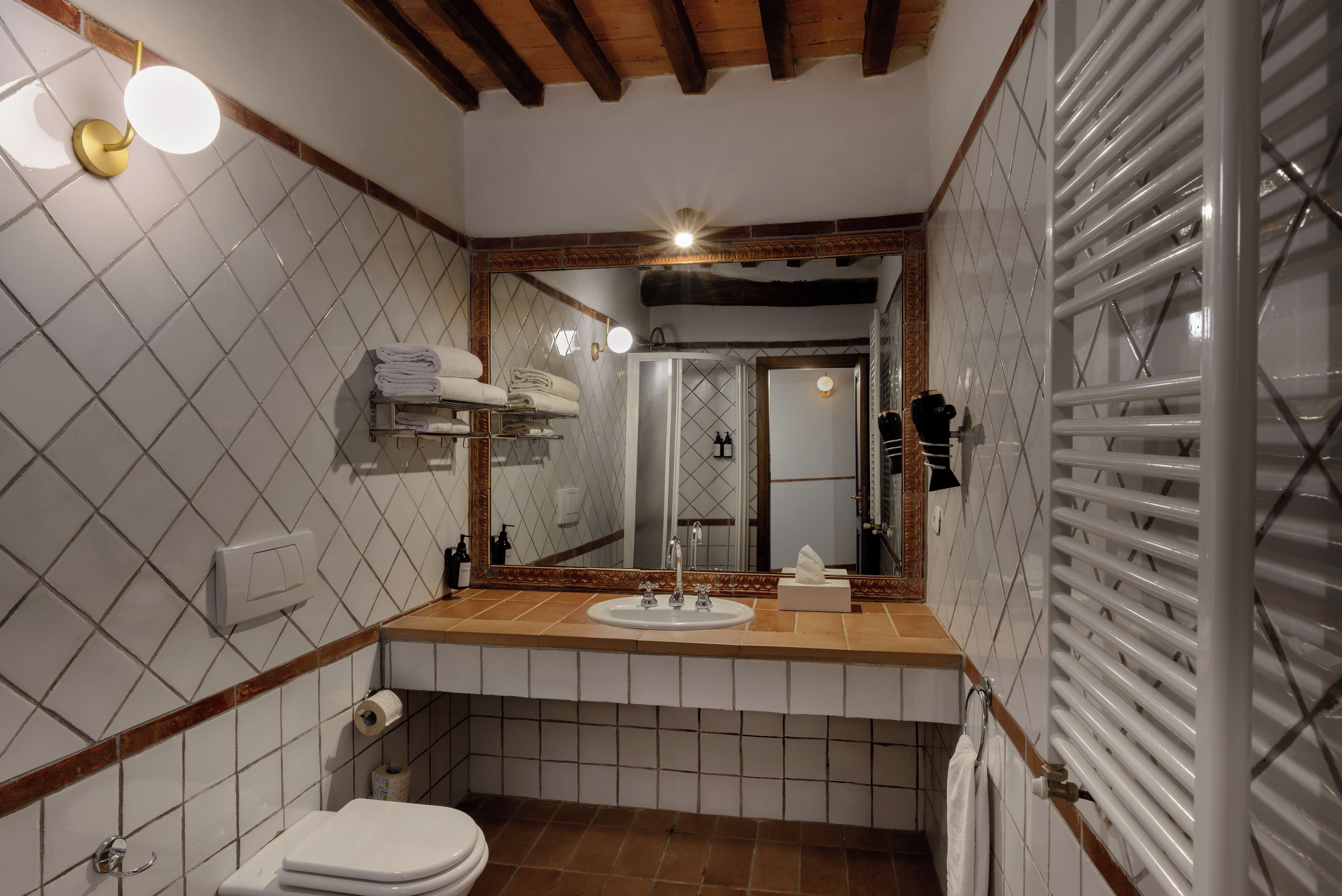 A bathroom with a toilet, sink, mirror, towel rack, and a shower area.