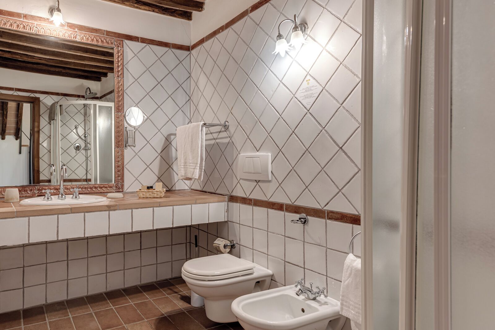 Un baño con lavamanos, inodoro, bidé y un espejo con una toalla colgada.