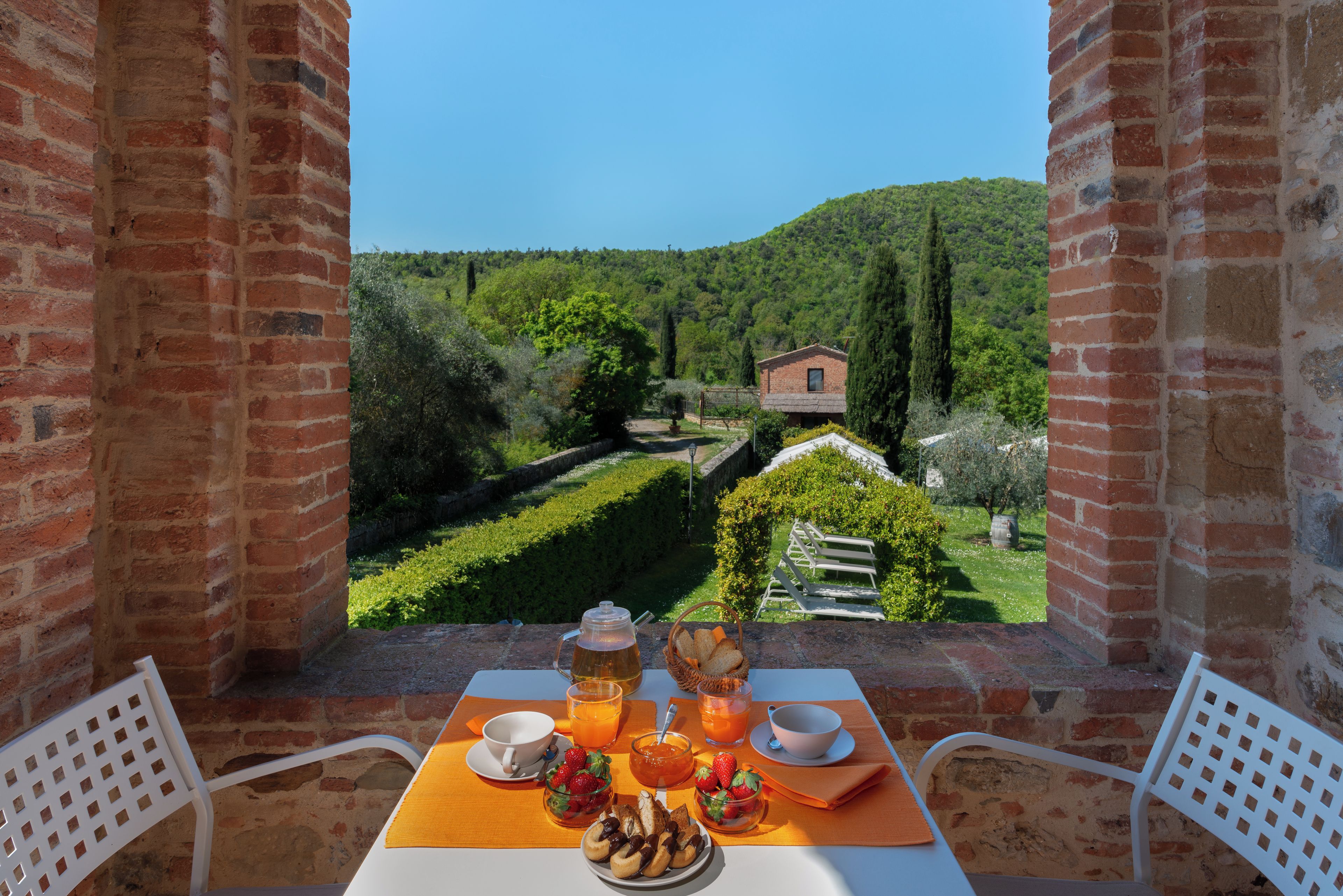 Una mesa dispuesta con alimentos para el desayuno, con vistas a un viñedo y un edificio rústico al fondo.