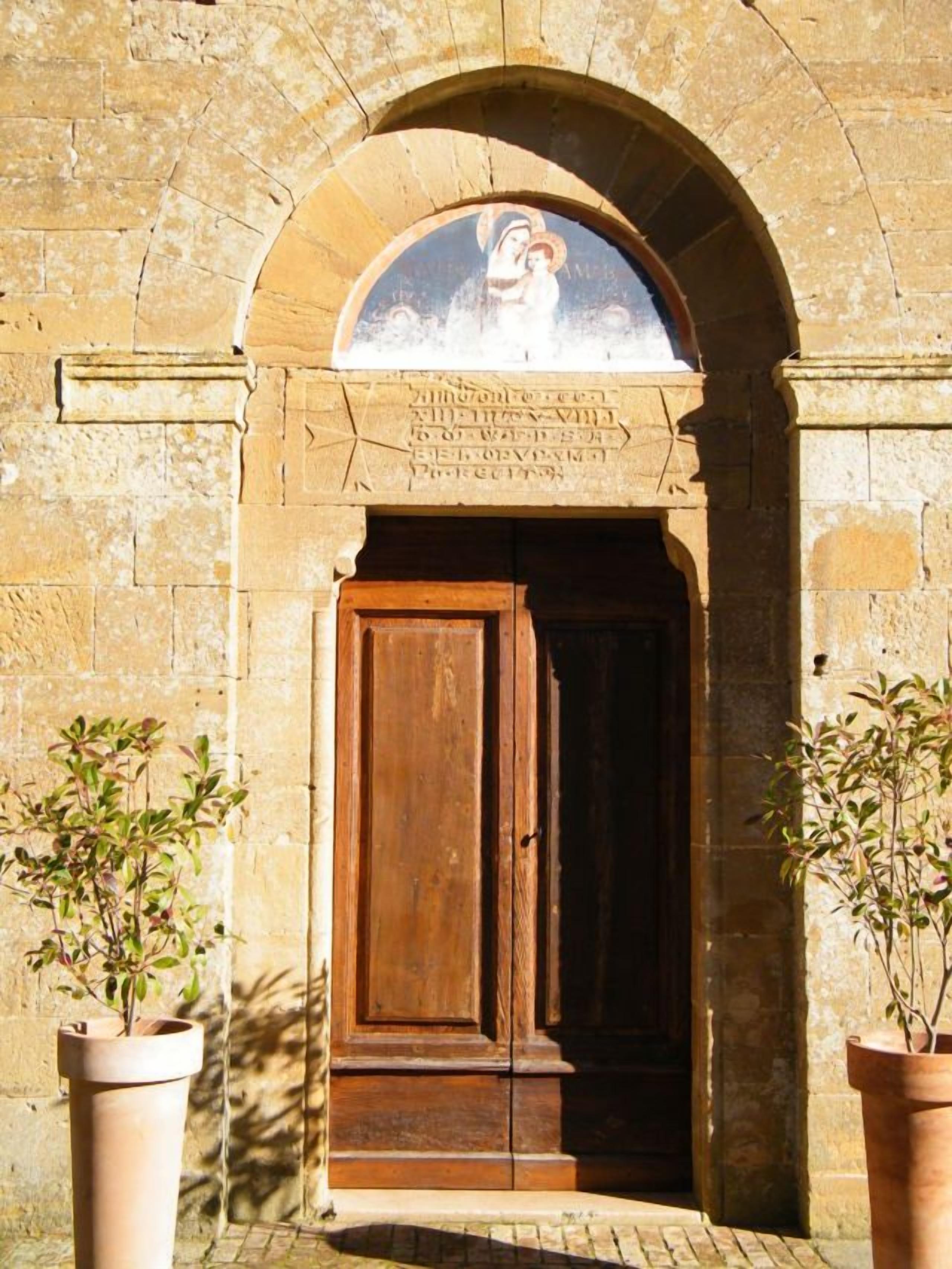 Una entrada arqueada con puerta de madera, flanqueada por macetas con plantas.