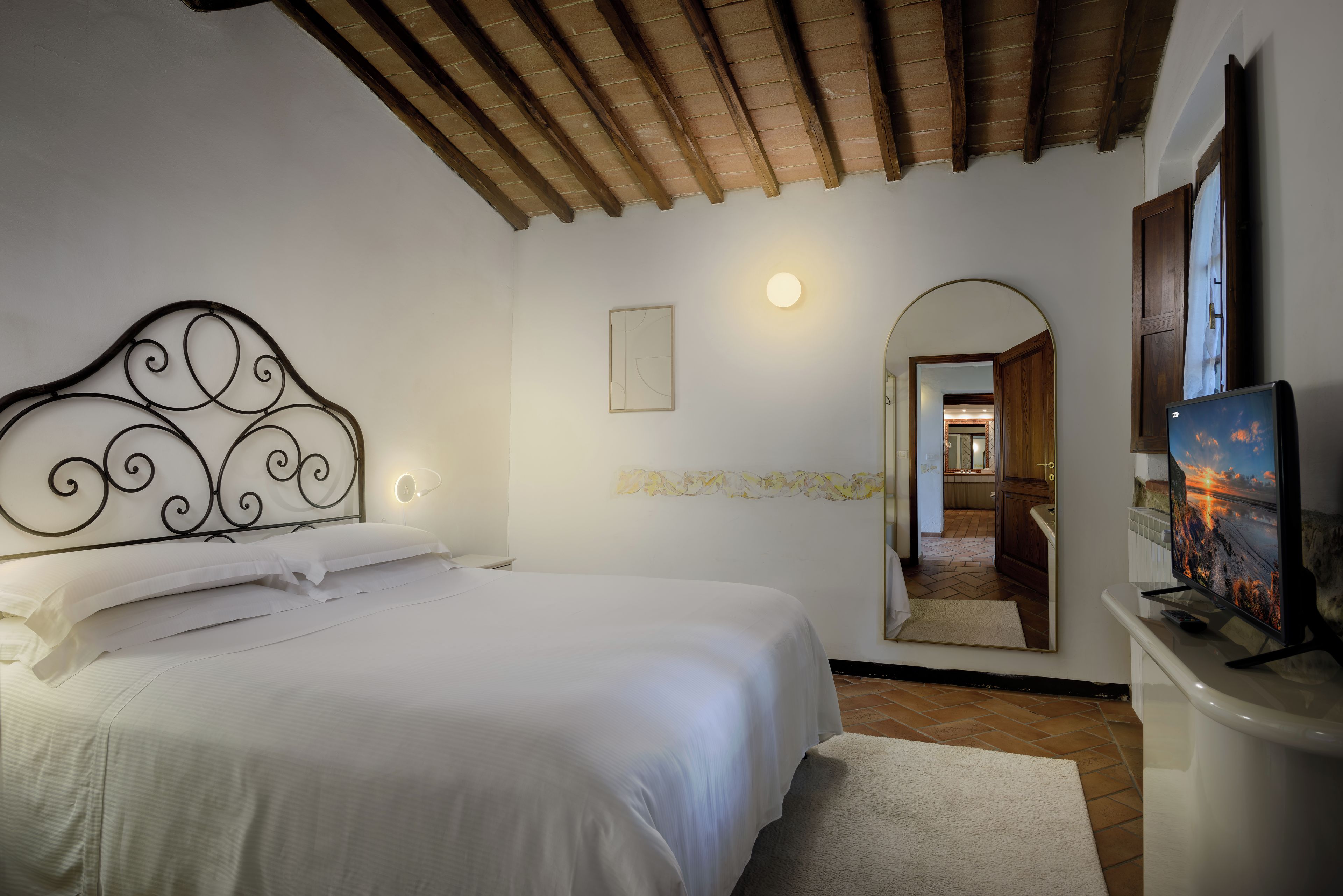Un dormitorio con cama, mesita de noche, televisor y espejo.