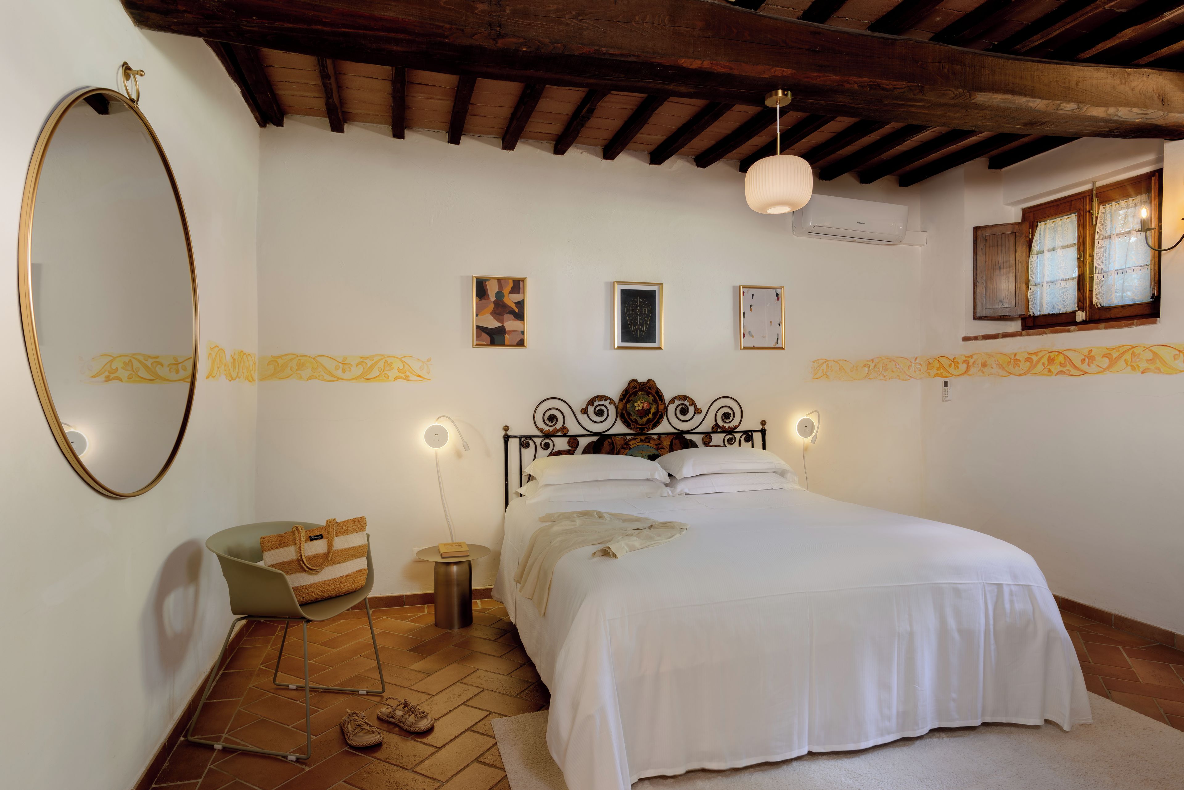 A bedroom with a bed, a mirror, a bedside table, a lamp, and a window with curtains.