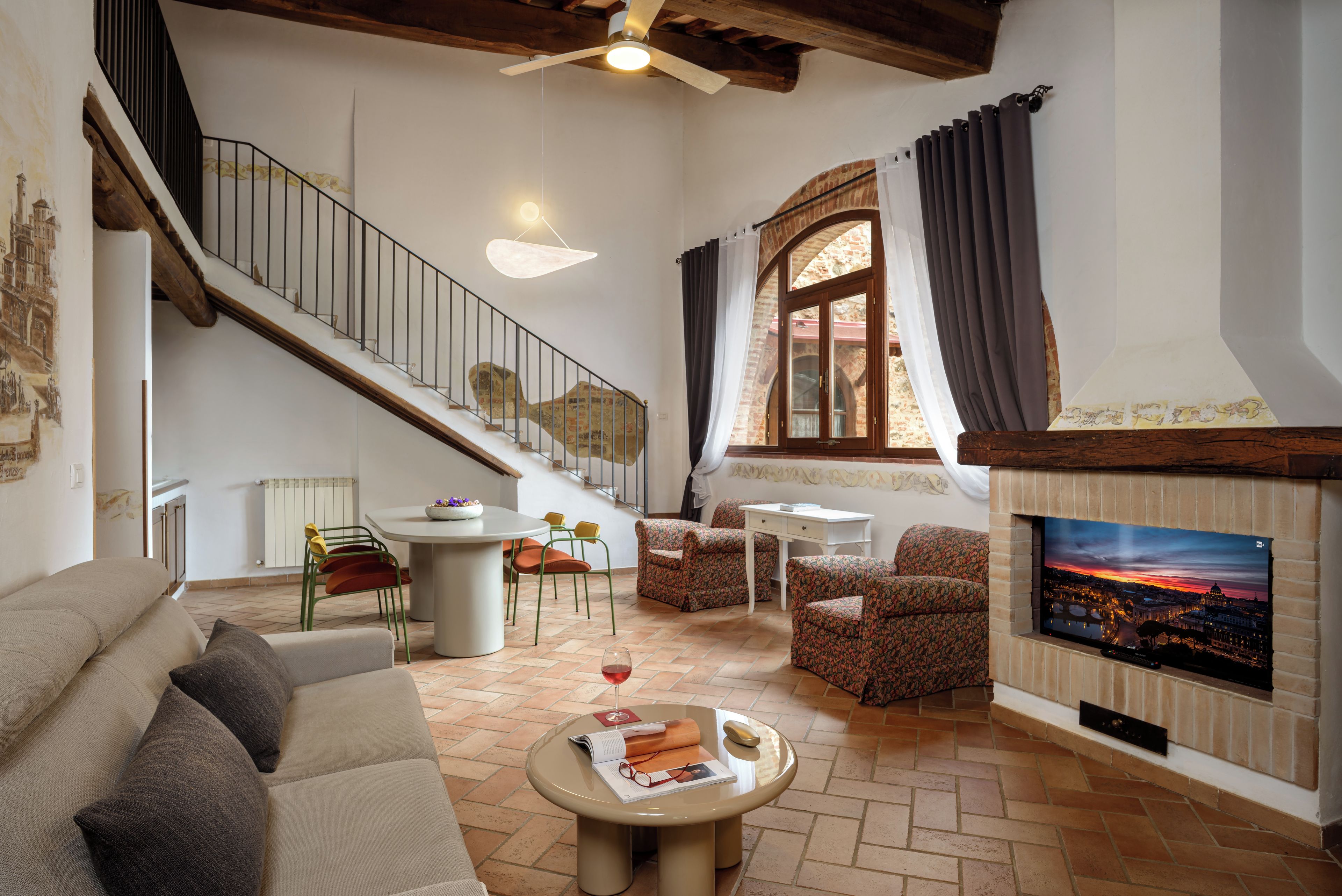 A spacious living room with a high ceiling, a fireplace, a dining area, and a staircase.