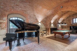A spacious room with a grand piano, a pool table, and a brick ceiling.