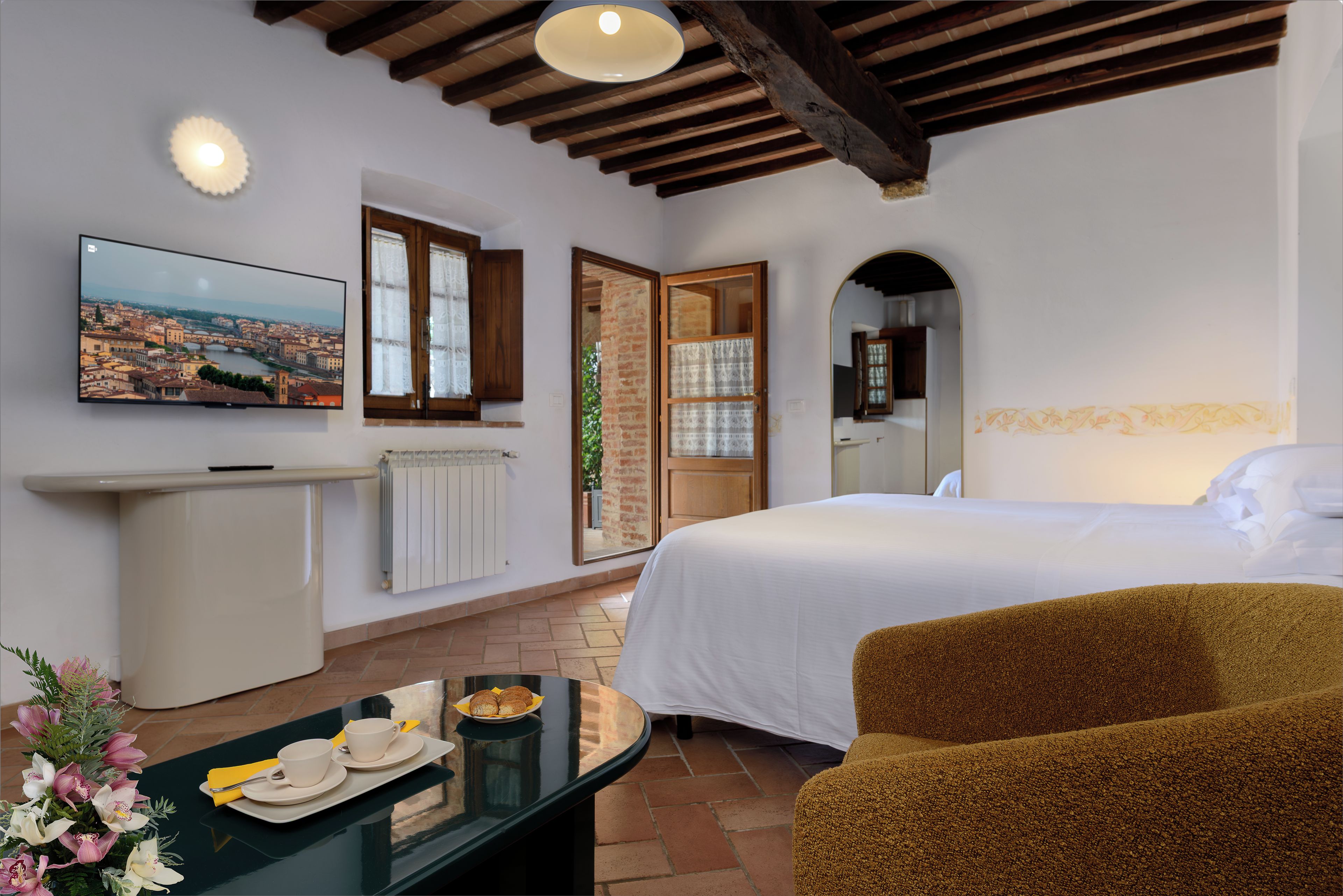 Habitación de hotel con cama, televisión, ventana con cortinas, espejo y mesa con bandeja de desayuno.