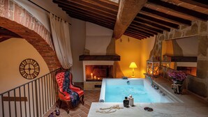 Un espace de détente avec un mur en pierre, un plafond en bois, un fauteuil rouge, une baignoire et un foyer.