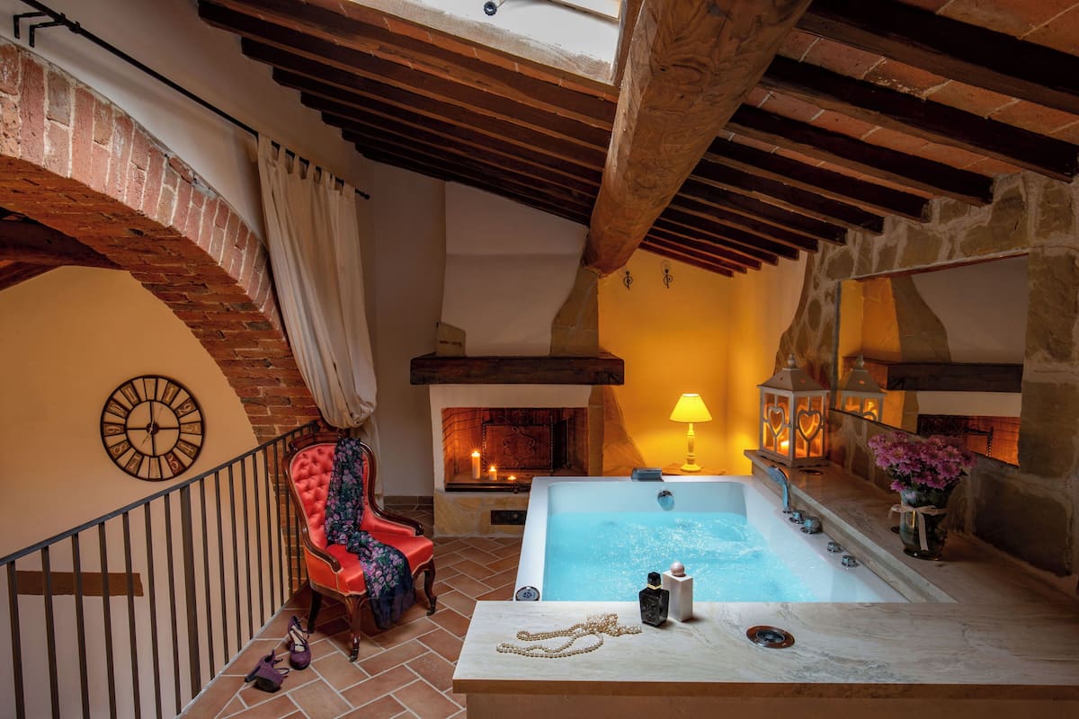 A spa area with a stone fireplace, a red chair, a wooden ceiling, and a bathtub.