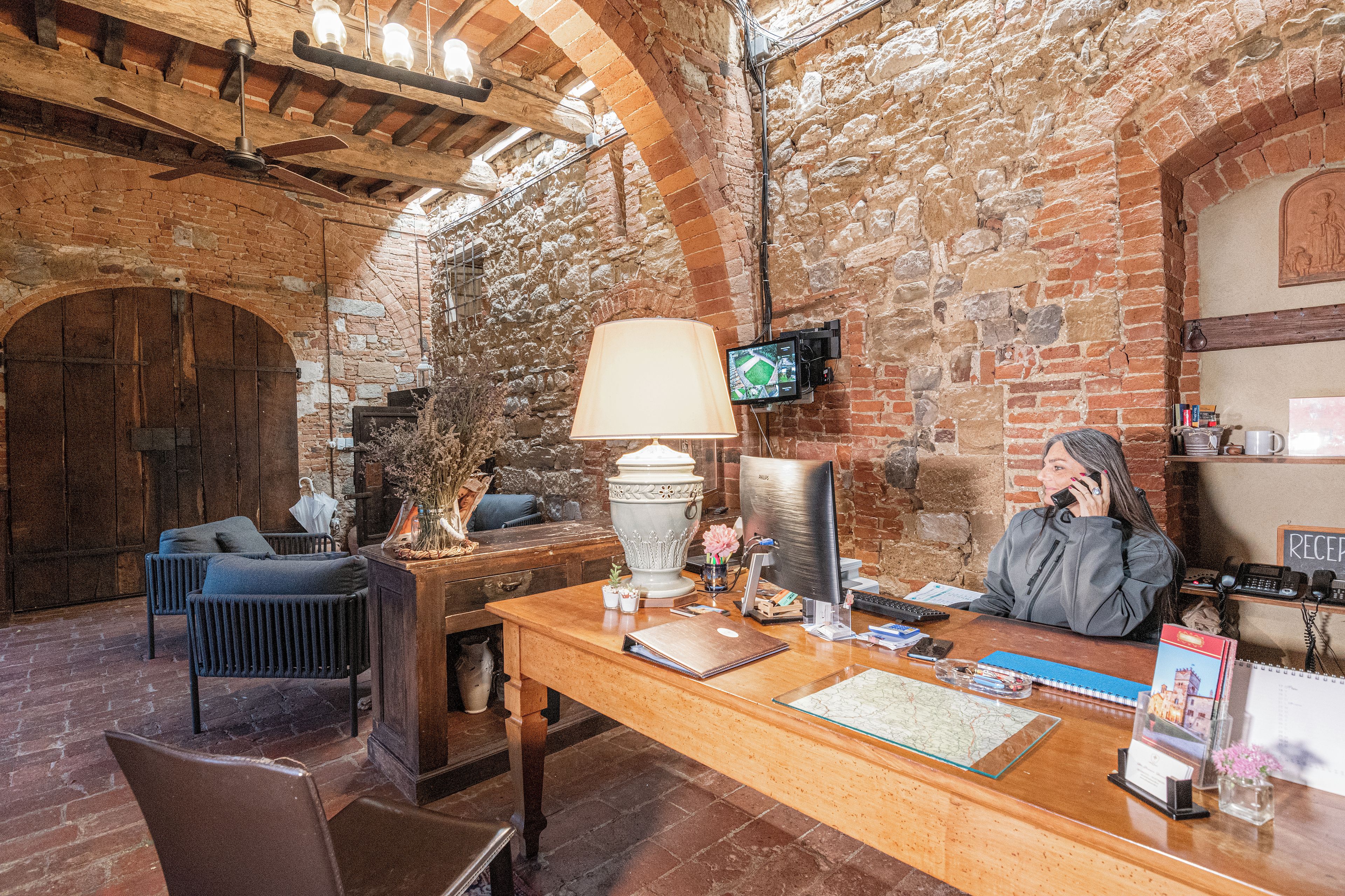 Un interior rústico con un mostrador de recepción de madera, una computadora, una lámpara y un televisor.