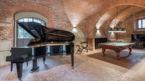 Une pièce spacieuse avec un grand piano, une table de billard et un plafond en briques.