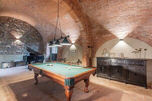 Una sala de billar con mesa de billar, un piano y una pared de ladrillo.