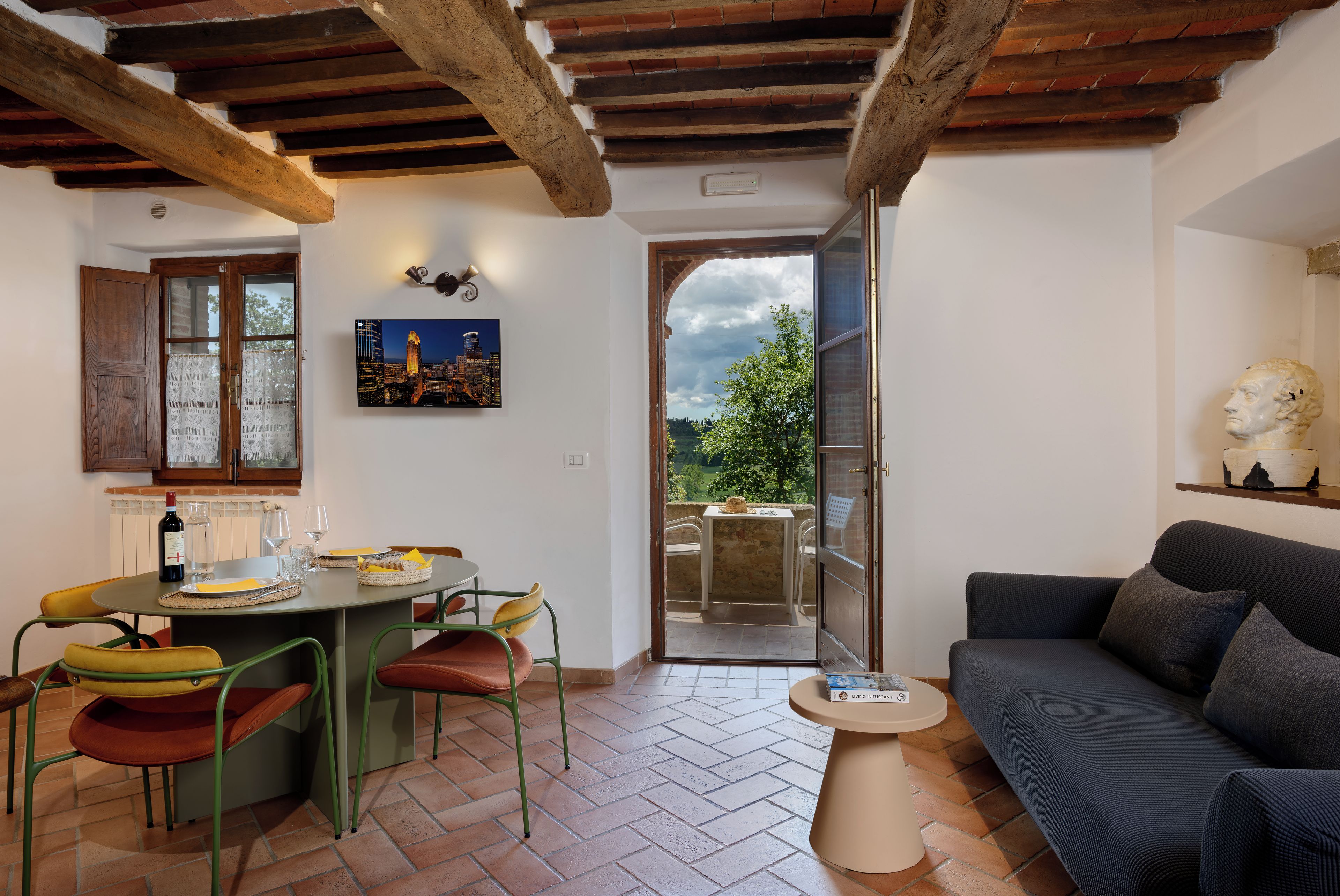 A room with a dining area, a sofa, and a view of the outdoors.