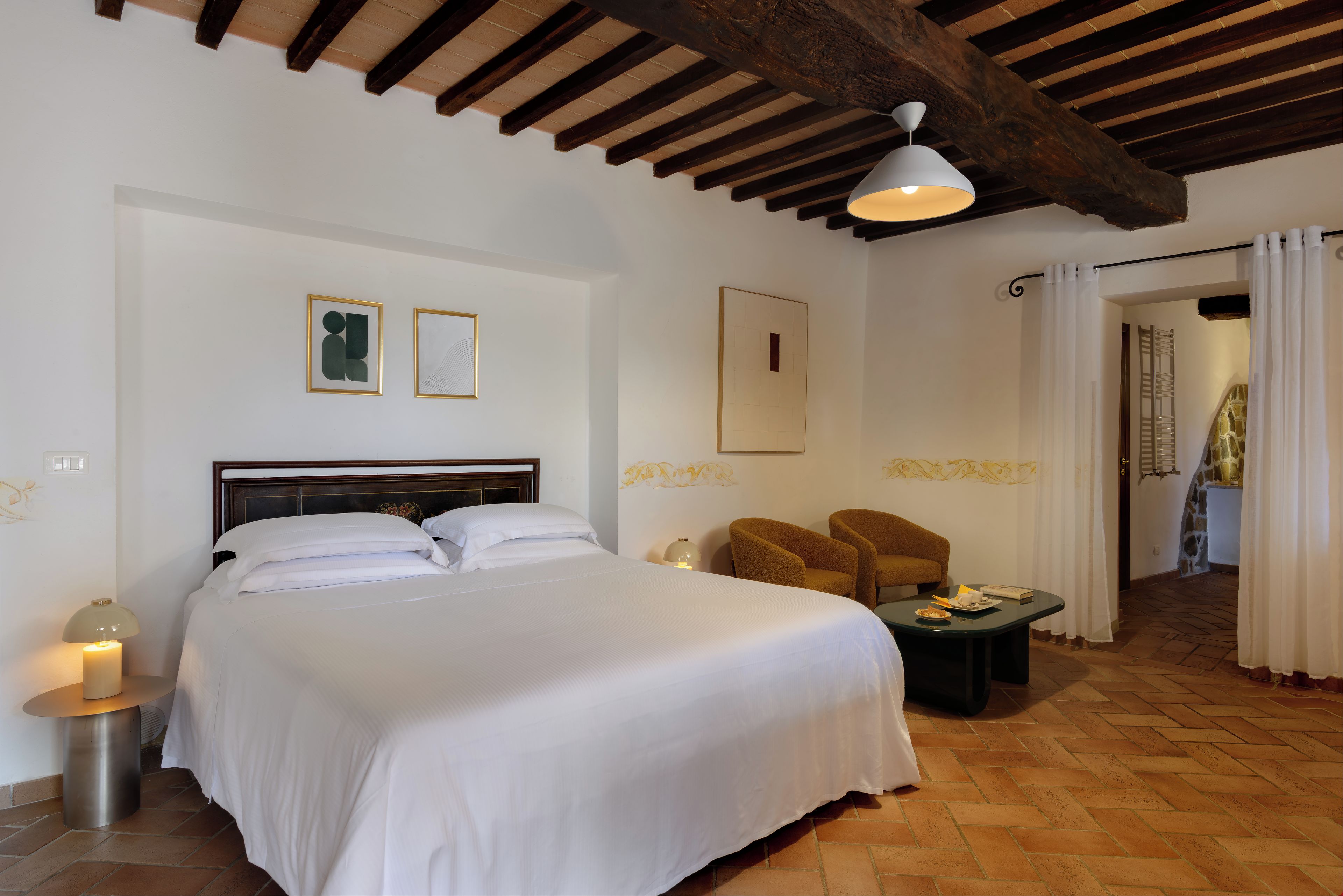 Una habitación de hotel con una cama grande, dos sillas, una mesita pequeña y un techo con vigas a la vista.