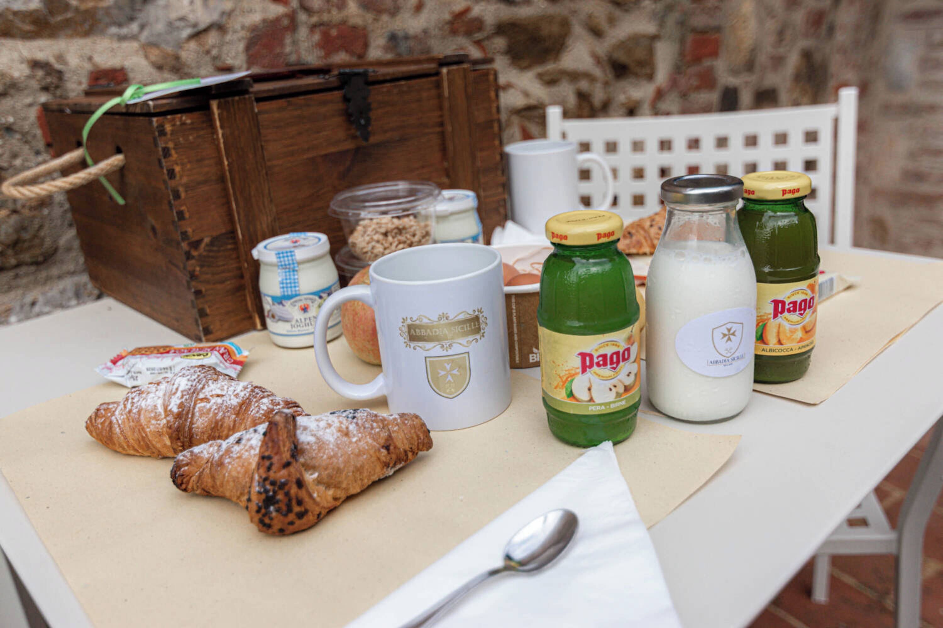 A table with croissants, a mug, milk bottles, and a jar of granola.