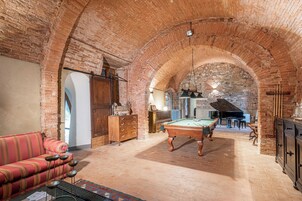Una habitación amplia con mesa de billar, sofá y un gran piano.